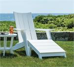 A White Contemporary Adirondack Chair with a Footstool and side table on the grass near a stone wall.